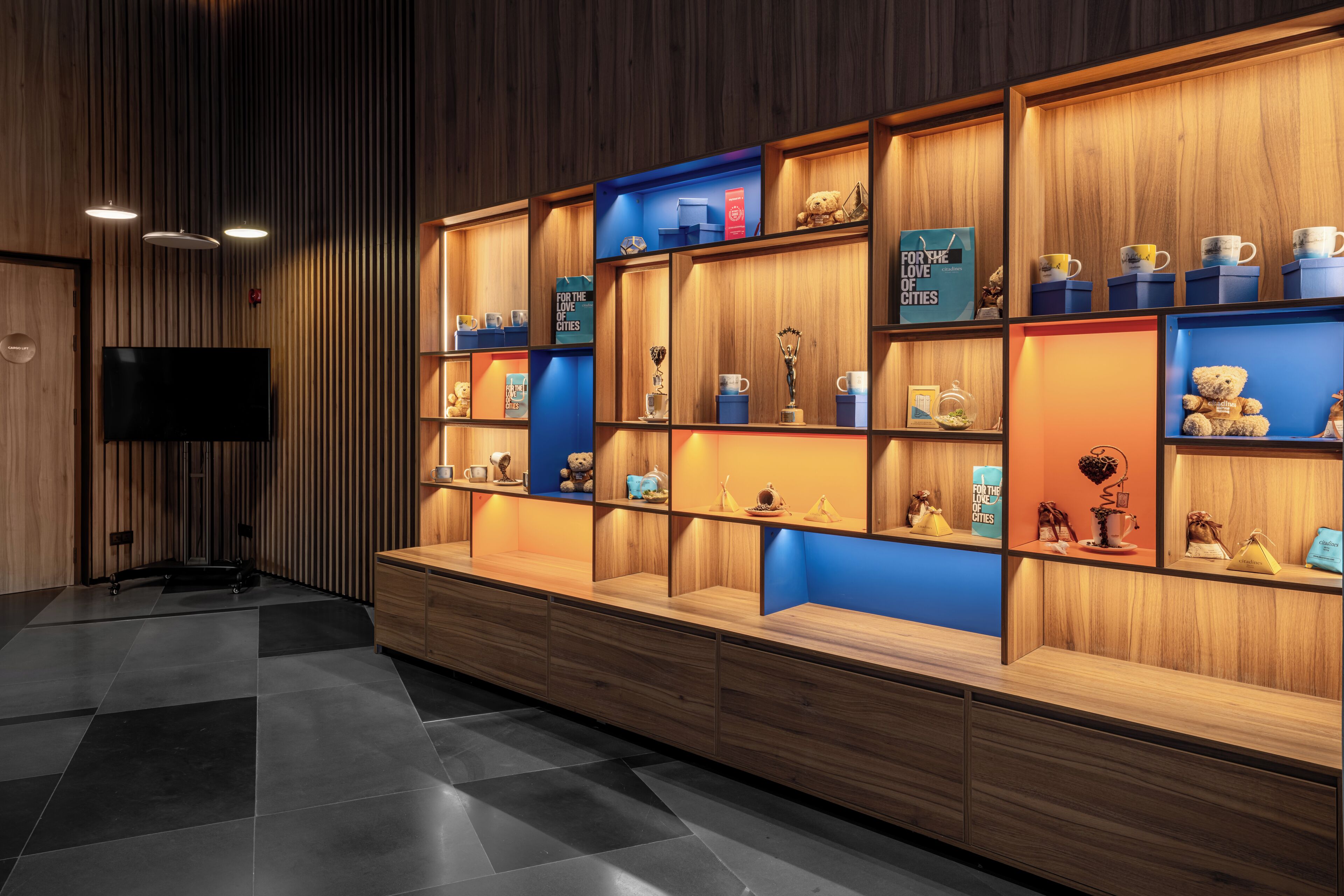 A hotel lobby with wooden paneling, a flat-screen TV, and shelves displaying trophies and souvenirs.