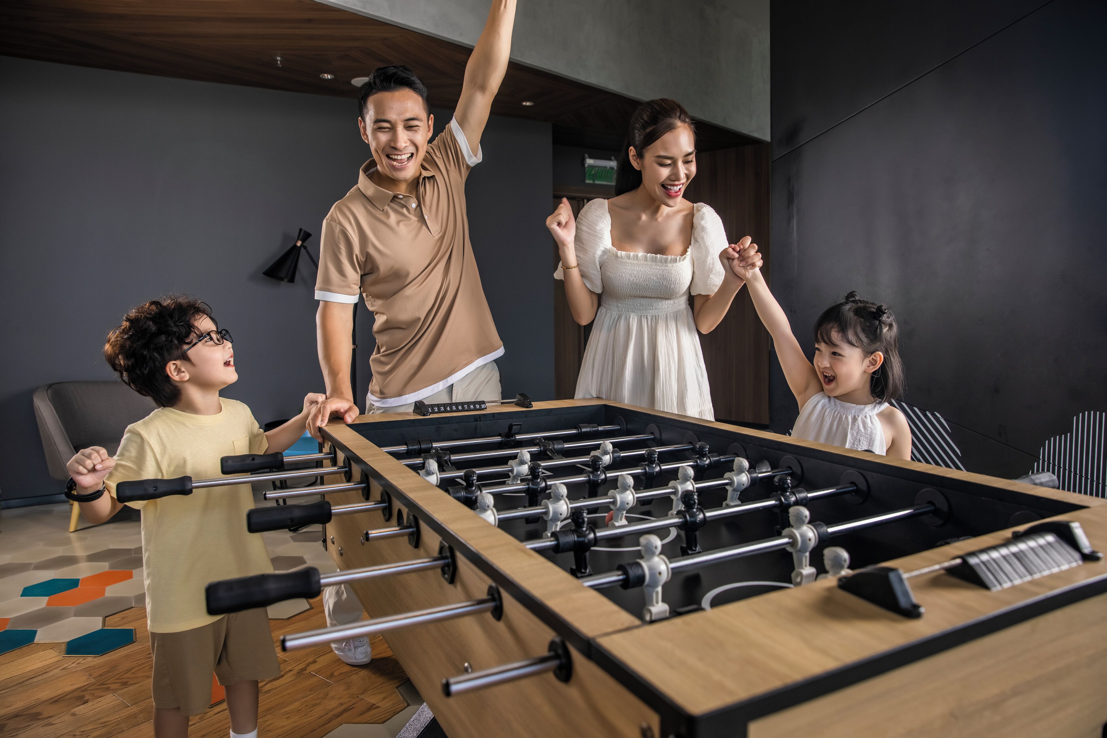 Una familia jugando al fútbol de mesa en una habitación moderna con suelo de madera y pared oscura.