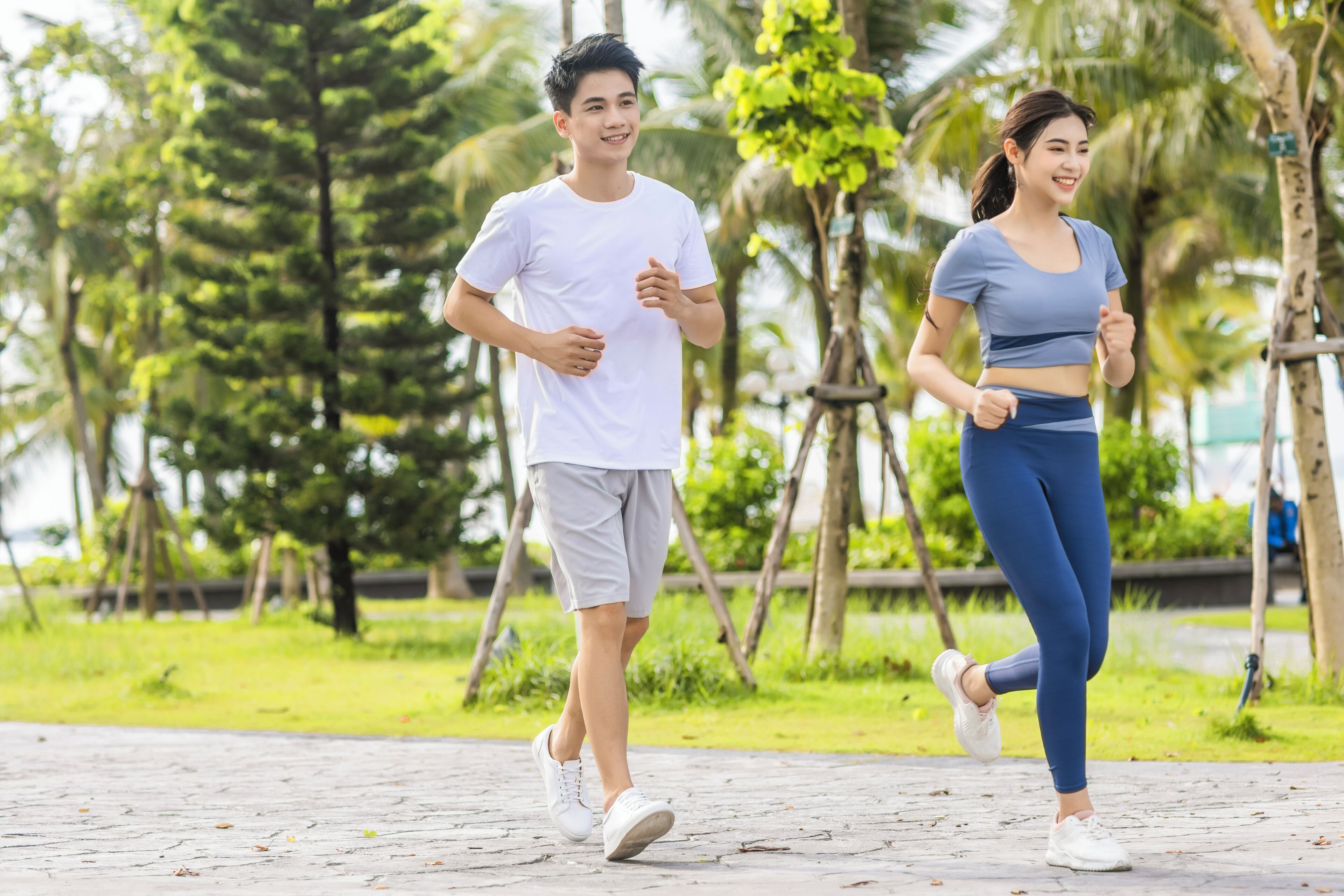 Two people jogging on a paved path in a park with trees and greenery in the background.