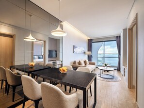A modern hotel room with a dining area, a sofa, a TV, and a view of the sea. - Citadines Marina Halong (Bai Chay)
