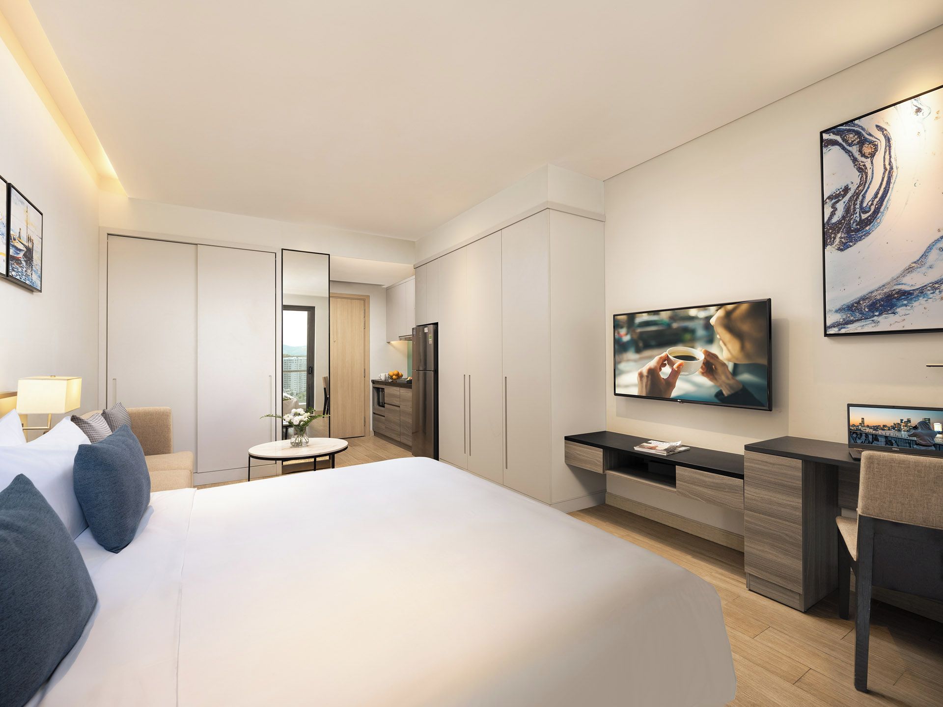 A modern hotel room with a large bed, a desk, a flat-screen TV, and a view of the city.