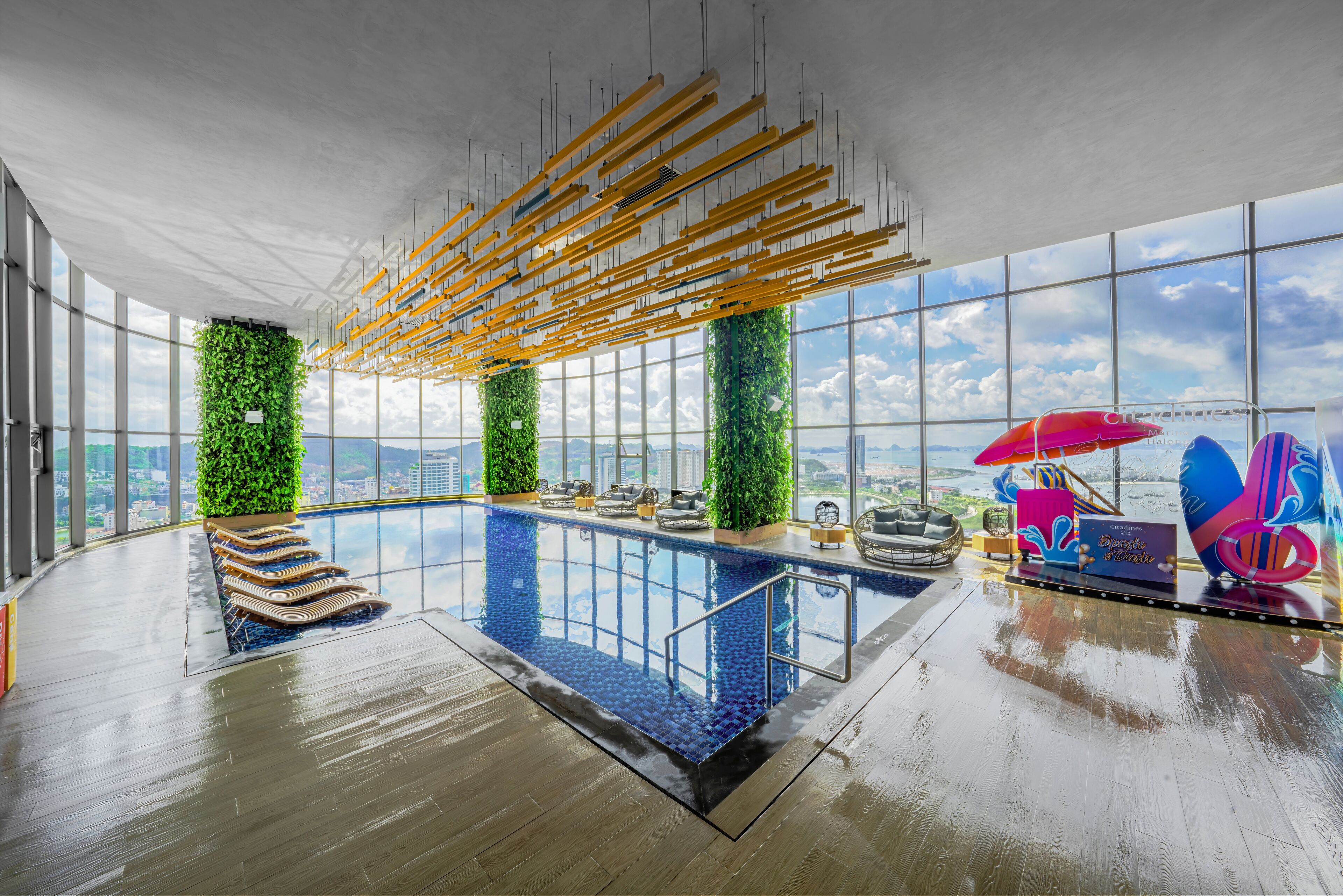 A modern indoor pool with a glass ceiling, green vertical gardens, and a view of the cityscape.