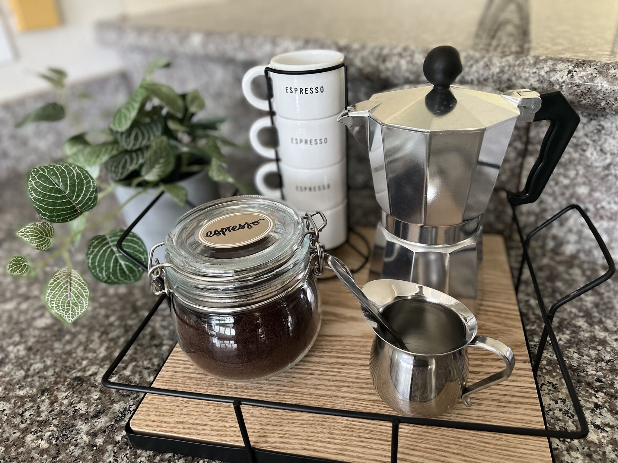 Un ensemble pour préparer le café comprenant un moulin, une cafetière à piston, une tasse et un bocal de café, le tout disposé sur un plateau en bois.