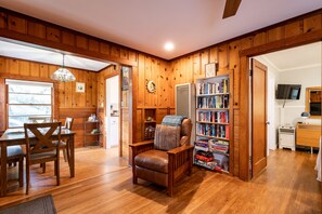 Una habitación acogedora con paredes de madera, una mesa de comedor con sillas, una estantería y un televisor.
