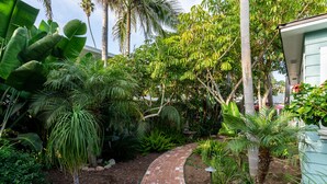 Un sendero de ladrillos que atraviesa un jardín exuberante con diversas plantas tropicales y palmeras.
