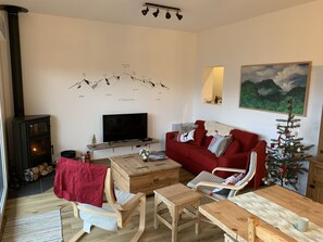 A cozy living room with a fireplace, a television, a red sofa, wooden furniture, and a Christmas tree.