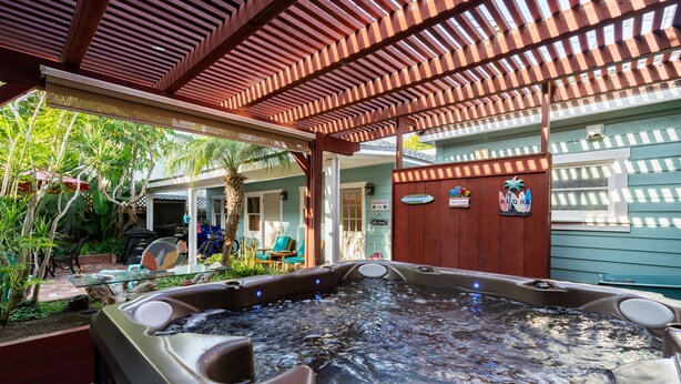 Ein Whirlpoolbereich mit einer hölzernen Pergola, umgeben von Grünpflanzen und einem Haus im Hintergrund.