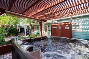 A hot tub under a wooden pergola with a view of a house and greenery. - OB Bungalow (San Diego)