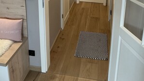 Un corridoio stretto con pavimento in legno, una porta bianca e un piccolo tappeto.