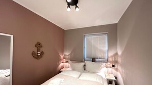 Una camera da letto con un letto, lampade sui comodini, una finestra con persiane, un lampadario e un elemento decorativo a parete.