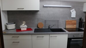 A modern kitchen with white cabinets, a black sink, a toaster, and a wooden cutting board. - Relaxation in the Ammergau mountains, centrally located (Oberammergau)
