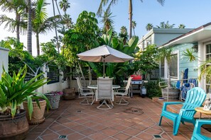 Un patio con una mesa y sillas, rodeado de plantas en macetas y un paraguas grande.