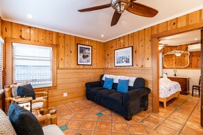 Una habitación acogedora con paredes de madera, un sofá azul oscuro con cojines azules, un banco de madera y una cama con edredón blanco.