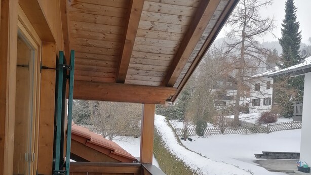 Un balcón de madera con muebles de mimbre y vistas a un paisaje nevado.