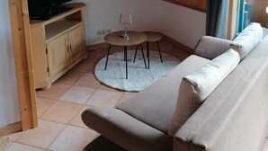 Un interior de madera con un sofá, un televisor sobre un mueble de madera y una mesita con un vaso.
