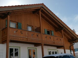 A wooden building with a balcony, large windows, and a tiled roof. - Comfortable 2 room apartment only 200 meters from the valley station. (Bad Kohlgrub)