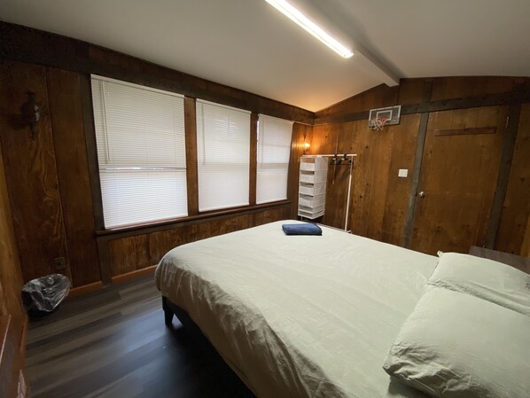 A bedroom with a bed, wooden walls, and a window with blinds.