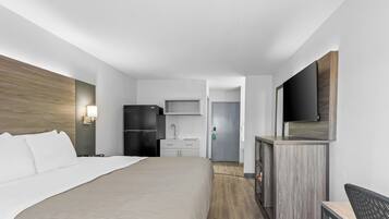 A hotel room with a bed, a desk, a refrigerator, a microwave, a sink, and a TV.