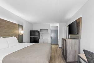 Habitación de hotel con cama, escritorio, refrigerador, microondas, lavamanos y televisión.