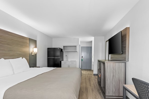 A hotel room with a bed, a desk, a refrigerator, a microwave, a sink, and a TV.