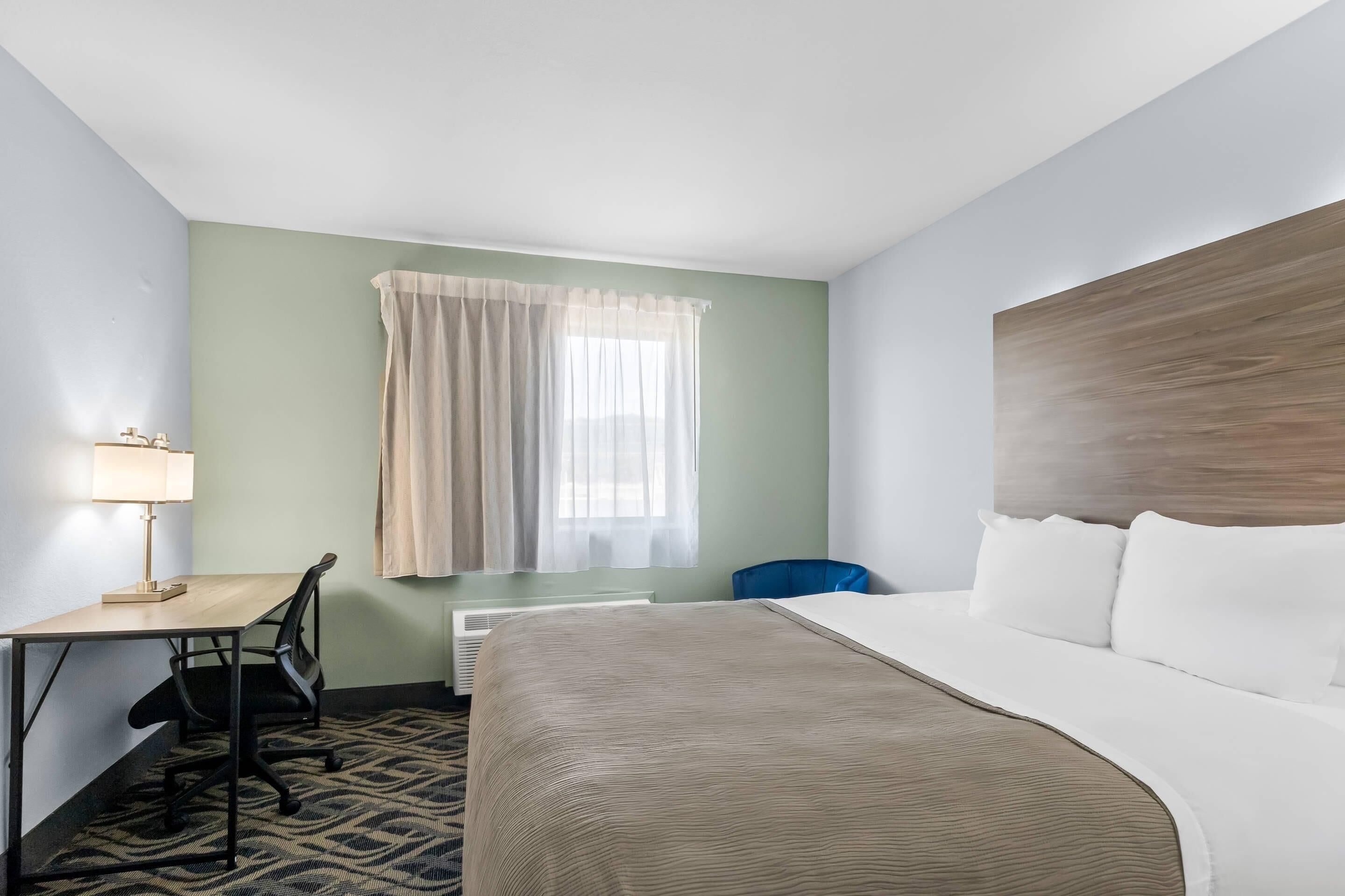 Habitación de hotel con cama, escritorio, silla y ventana con cortinas.