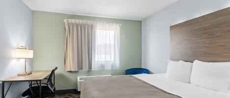 Habitación de hotel con cama, escritorio, silla y ventana con cortinas.