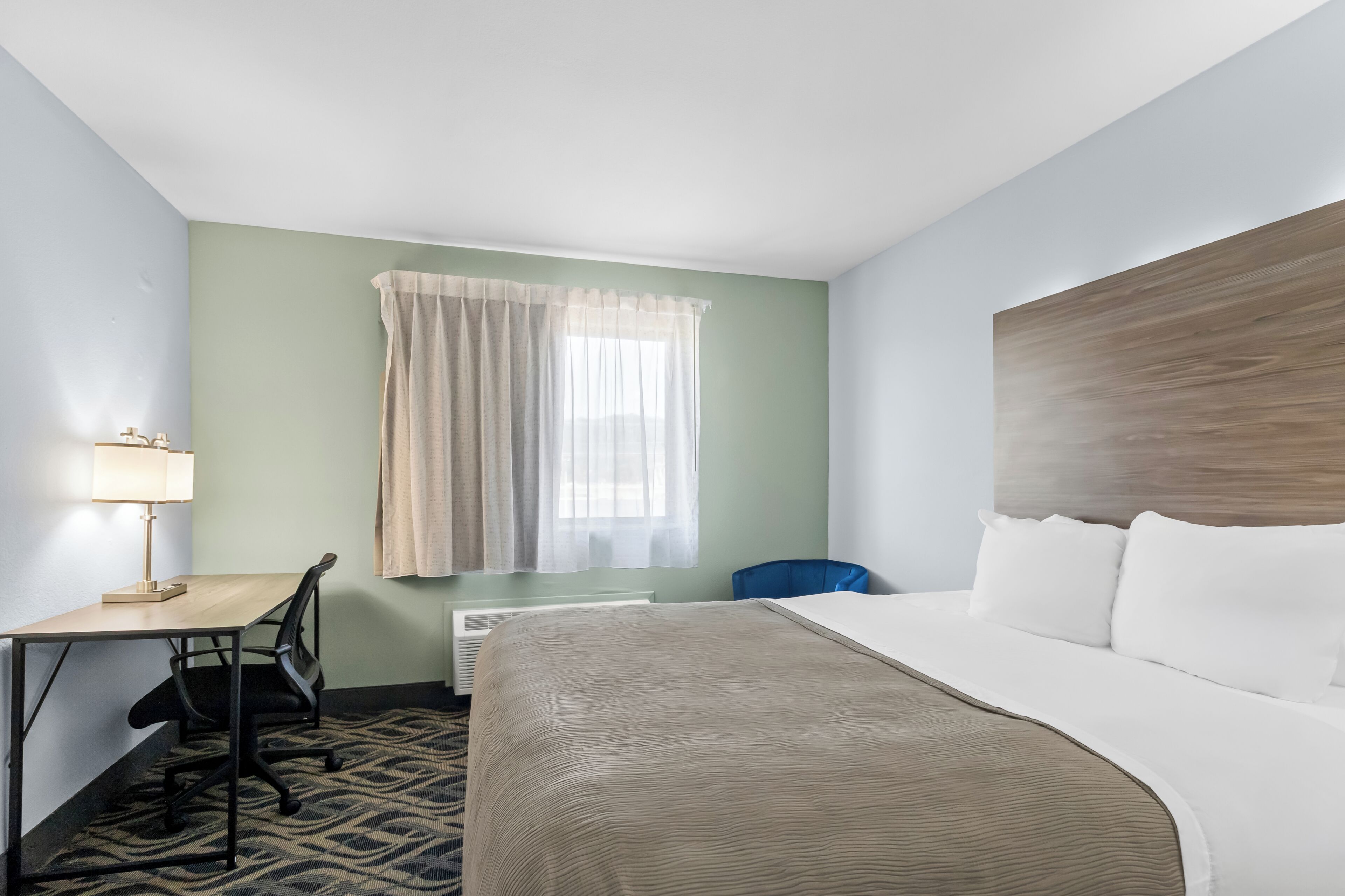 Une chambre d’hôtel avec un lit, un bureau, une chaise et une fenêtre avec des rideaux.