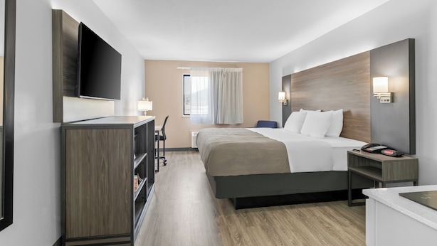 A hotel room with a bed, bedside tables, a desk, a chair, a TV, and a window with curtains. - Quality Inn (New Martinsville)