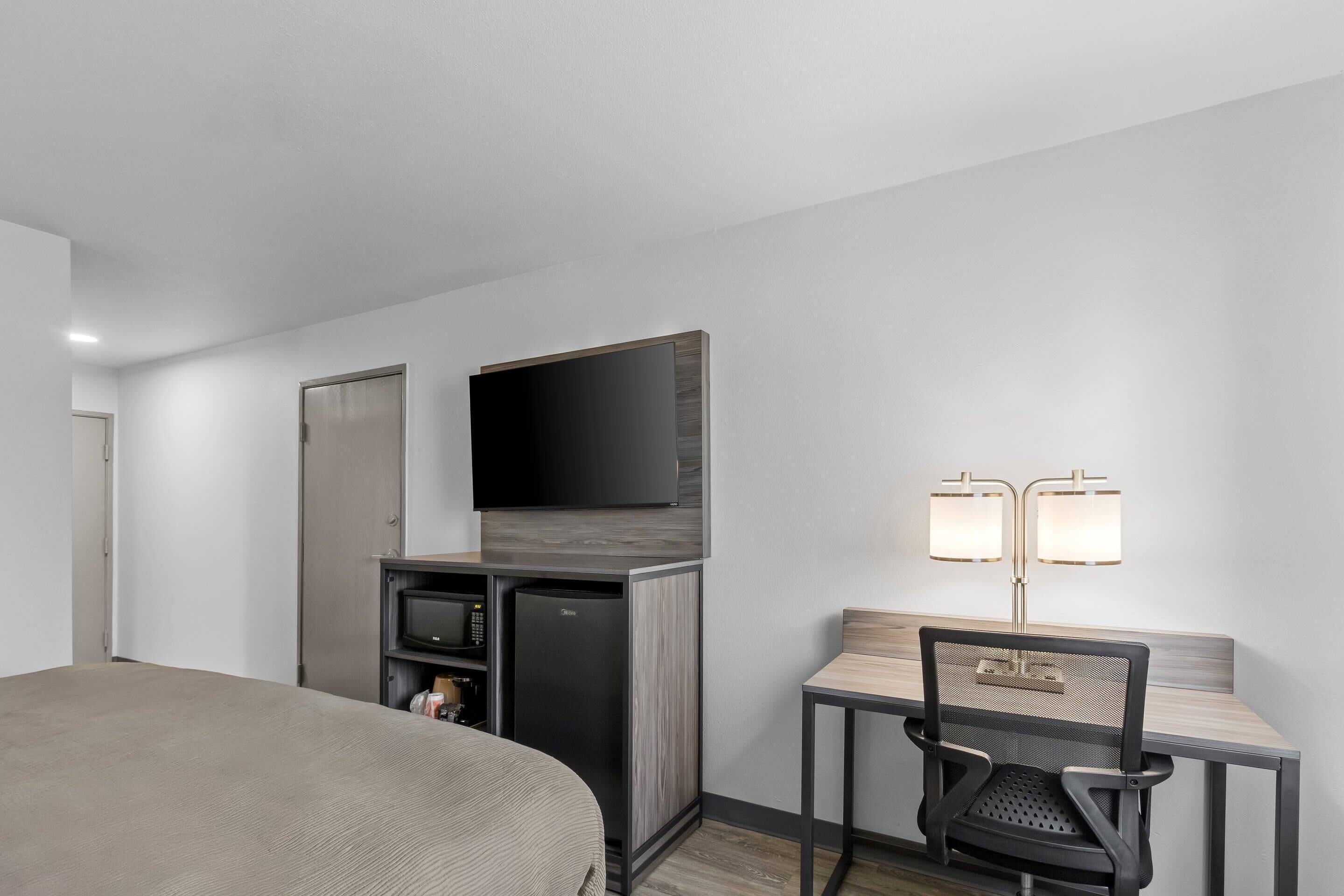 A hotel room with a bed, a desk with a chair, a television, a minibar, and two wall-mounted lamps.