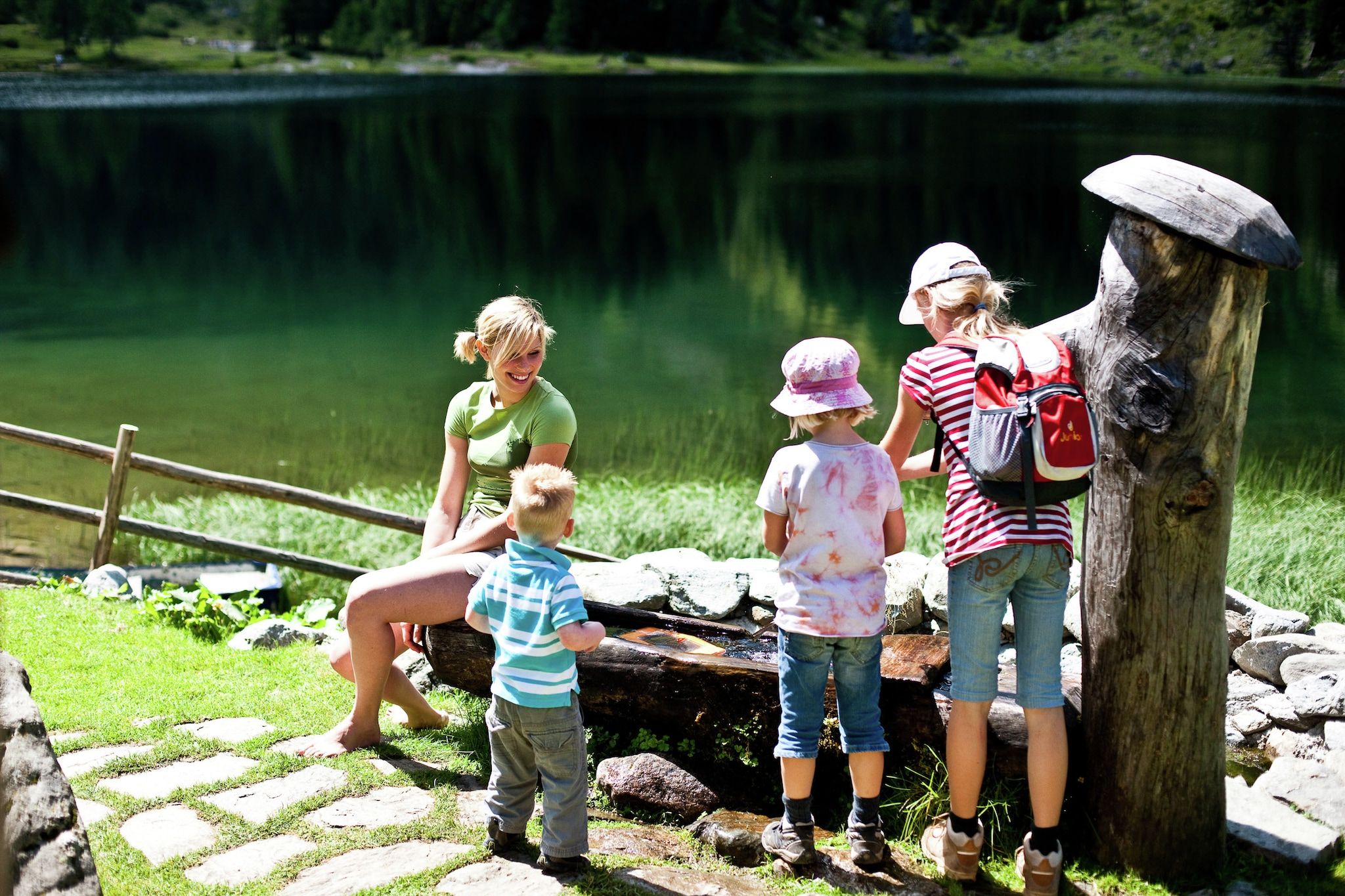 A group of people near a lake with a wooden structure and a stone path.