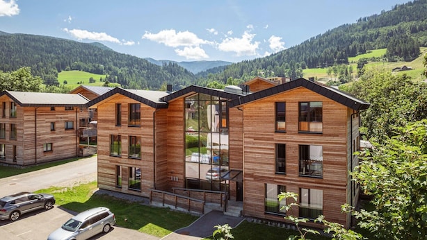 Un edificio moderno in legno con diversi piani, ampie finestre e vista su un paesaggio montano.