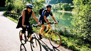 Two cyclists on a paved path beside a lake, surrounded by greenery.