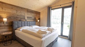 Una camera da letto con un letto grande, pareti in legno a pannelli, un piccolo tavolino rotondo e una porta scorrevole in vetro che si apre verso l'esterno.