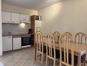 A compact kitchen with a dining area, including cabinets, a microwave, a coffee maker, and a dining table with chairs.