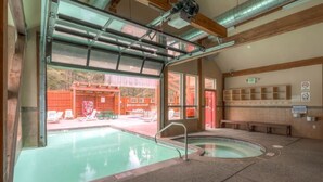 En swimmingpool med et glasafskærmning, bænke og udsigt over et udendørs område med et rødt hegn og liggestole.
