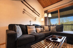 A cozy living area with a sectional sofa, a wooden coffee table, and skis mounted on the wall. - Sundowner Mountain View Condo • Walk to Slopes & Main St  • Pool Access (Breckenridge)