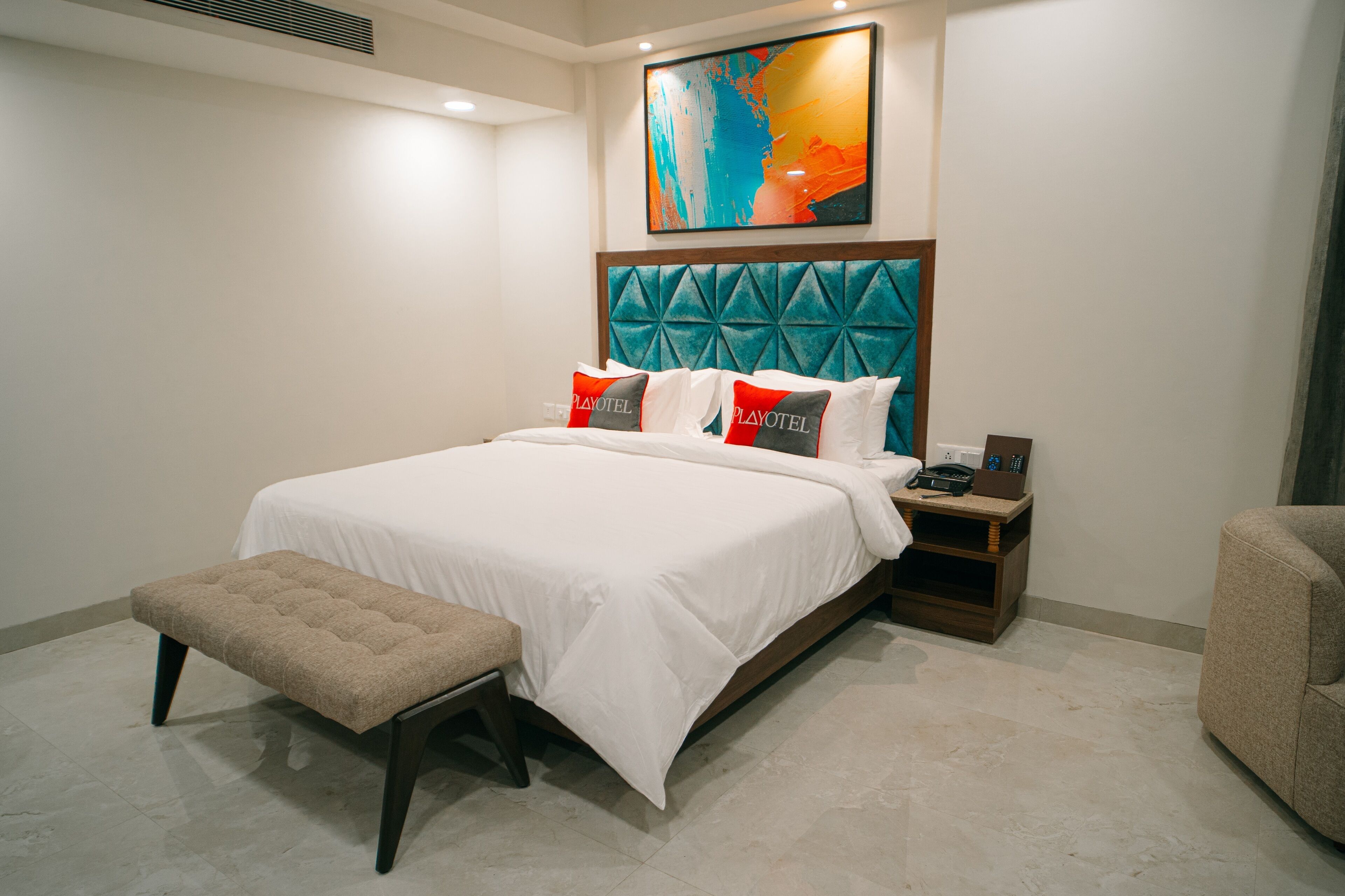 A neatly arranged bedroom with a large bed, a bench, a nightstand, and a wall-mounted artwork.