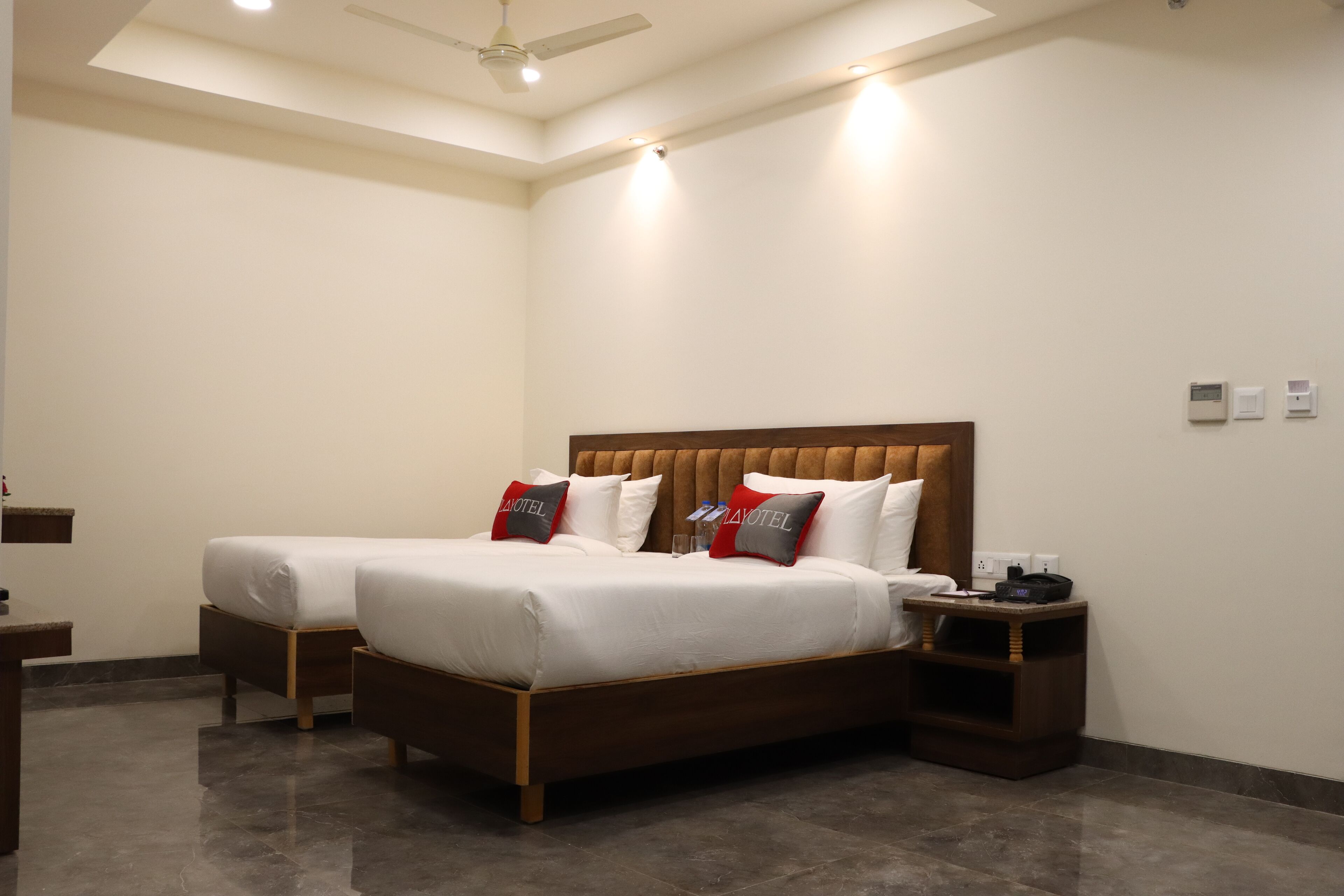 Habitació d'hotel amb un llit gran, un llit més petit, una taula de treball i una tauleta de nit.