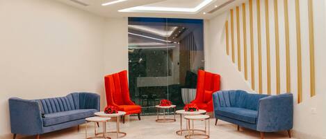 A modern lobby with two blue sofas, red chairs, and small round tables with red flowers.