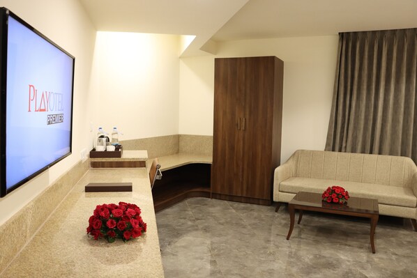 Habitación Playotel Premier con televisor, sofá, mesa de centro con un ramo de rosas rojas, armario de madera y suelo alfombrado.