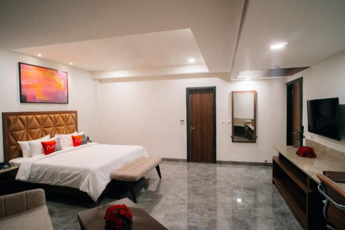 Ein Hotelzimmer mit Bett, Sitzbank, Fernseher, Spiegel und einem Bild an der Wand.
