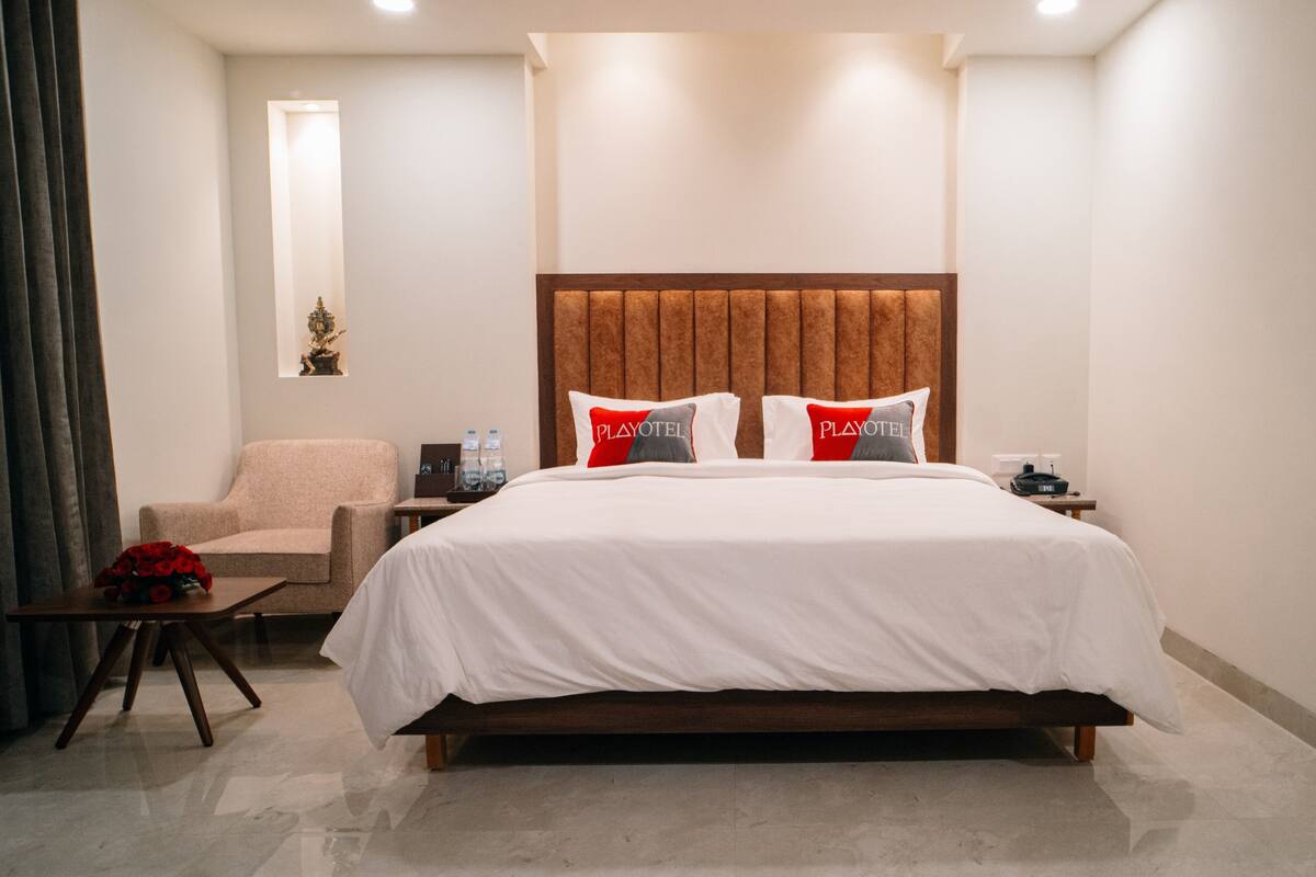 Ein Hotelzimmer mit einem großen Bett, einem Sessel, einem kleinen Tisch und einem Nachttisch.