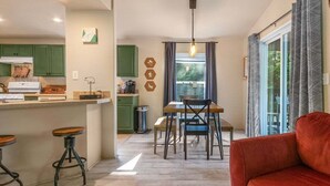 Een kleine keuken met groene kastjes, een eethoek met tafel en stoelen, en een rode bank in een zithoek.
