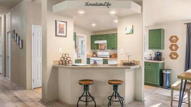 Een moderne keuken met groene kastjes, een centraal eiland met krukken en een bord met de tekst 'MountainLife'.