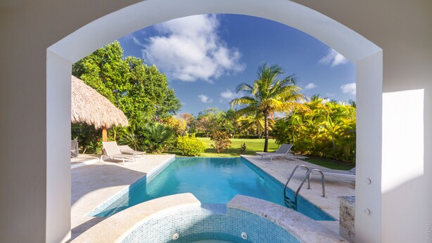 Une piscine avec un jacuzzi, entourée de chaises longues et de palmiers.