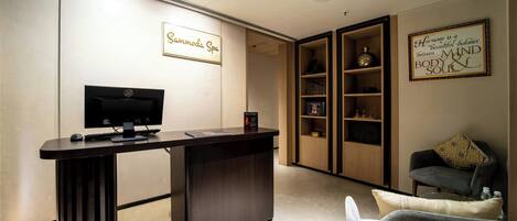 A reception desk with a sign reading "Sannmuda Spa," a television, and a shelving unit with decorative items.