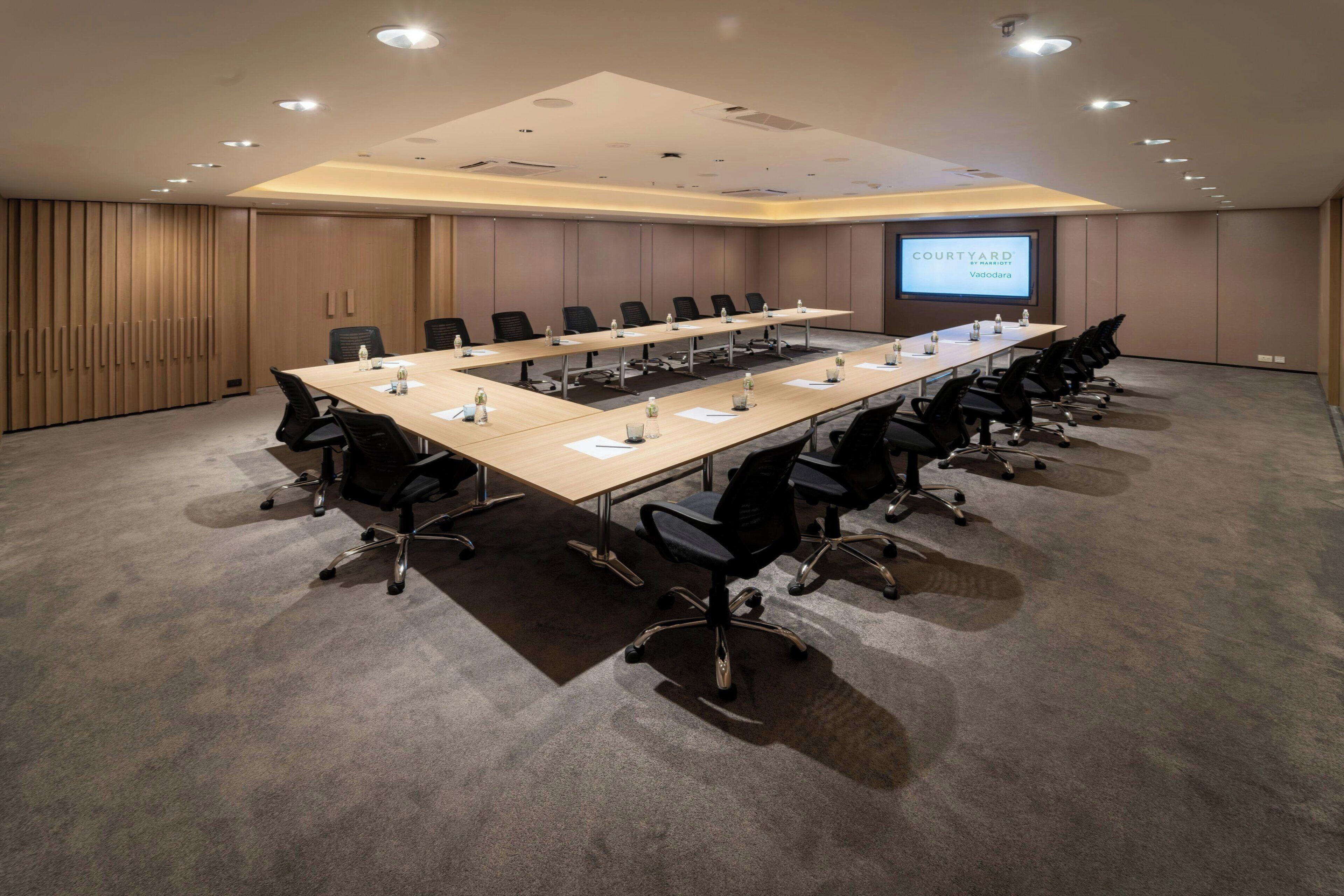 A conference room with a long table, multiple chairs, a projector screen, and a carpeted floor.