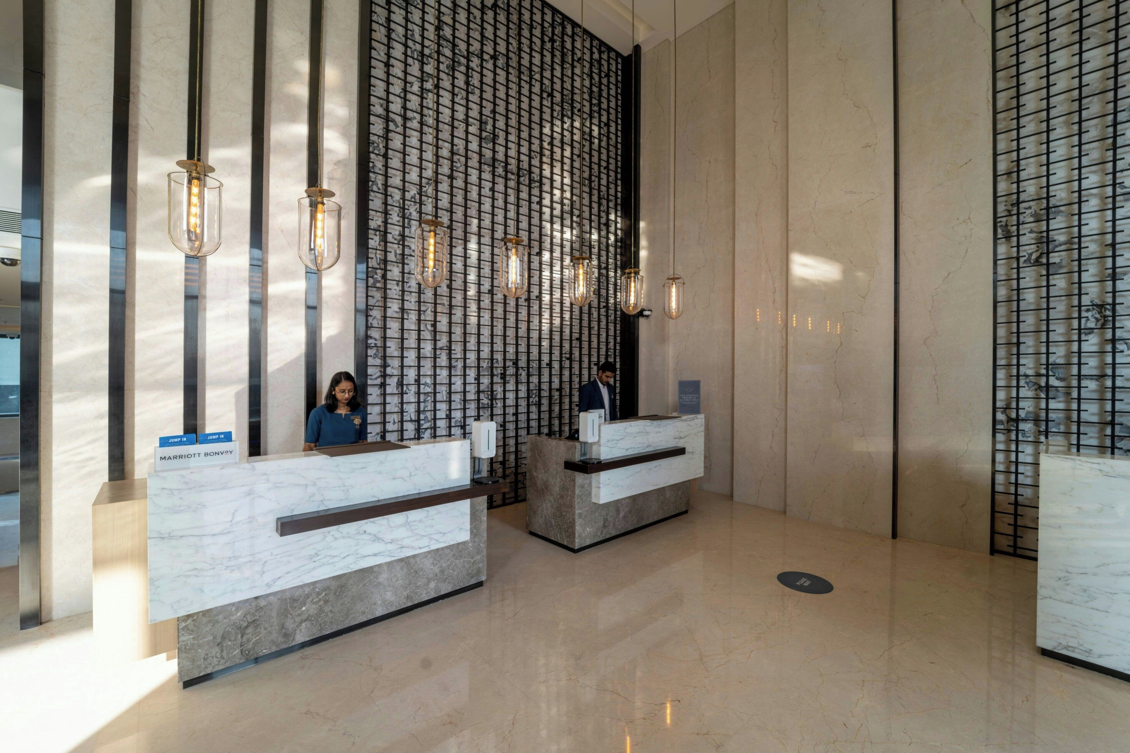 A hotel reception area with marble counters, a vertical light fixture, and a patterned wall.