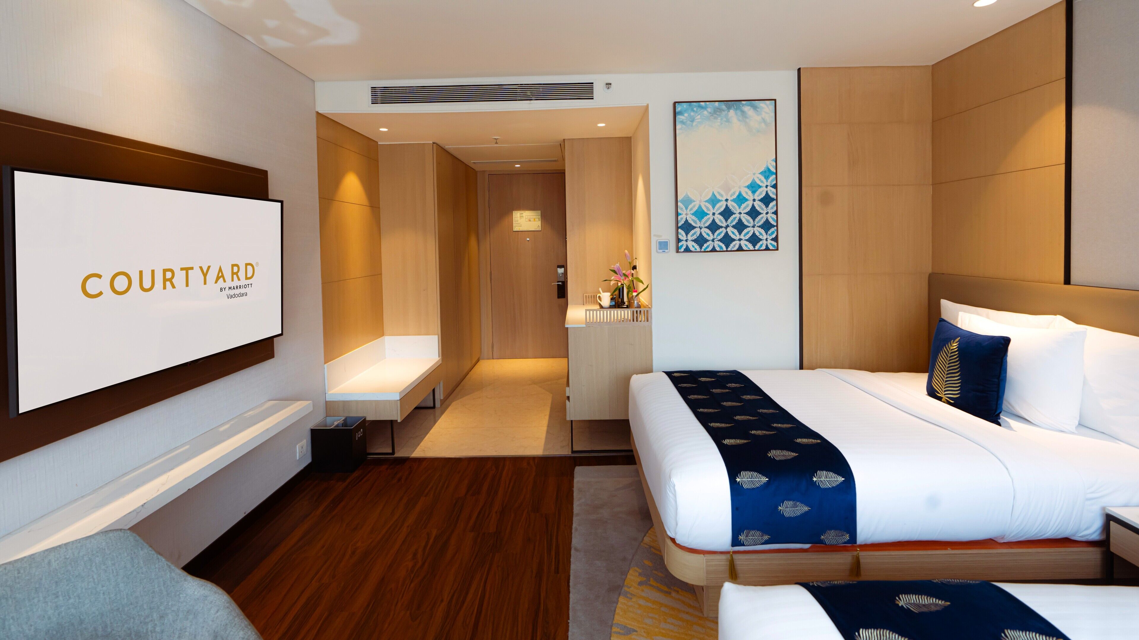 A modern hotel room with a large bed, a bedside table, a desk, and a seating area.