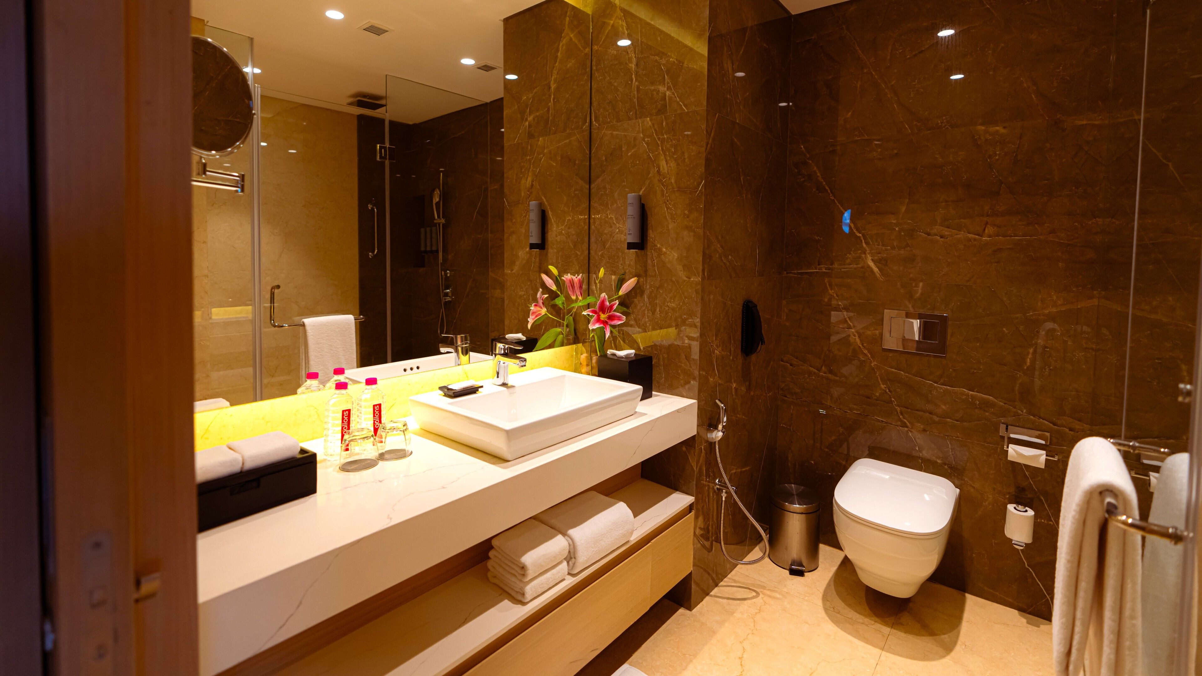 A modern bathroom with a large mirror, a white sink, a toilet, and a shower area.